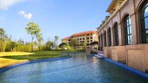 A hotel with a swimming pool, greenery, and a building with arched windows. - Yourworld International Conference Center (Jinhua)