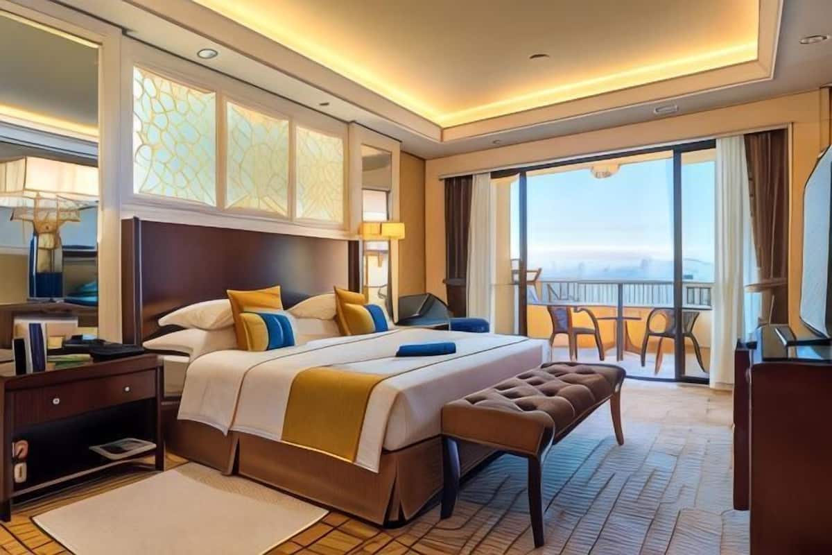 A hotel room with a large bed, a bench, a desk, and a balcony with a view.