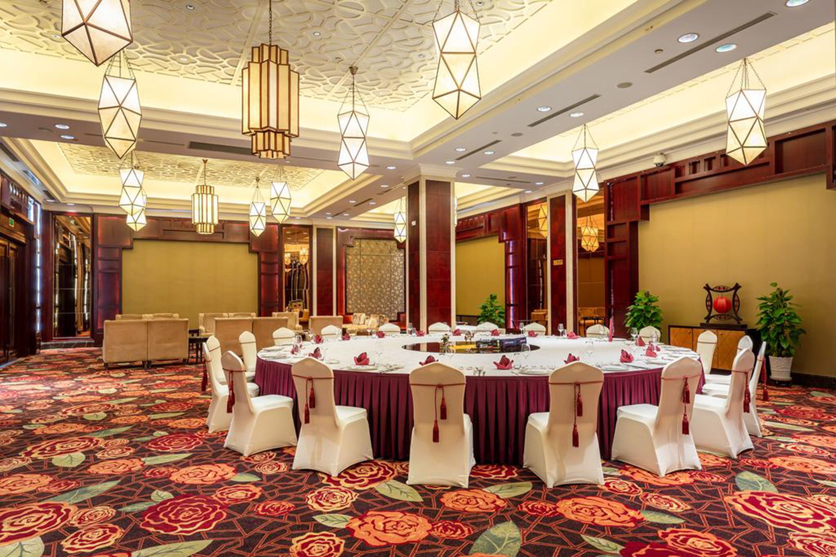 A banquet hall with round tables, white chairs, and a patterned carpet.
