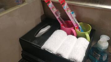 Un baño con una caja de pañuelos negros, una taza rosa y otra verde, una botella azul de jabón para manos y una toalla blanca.