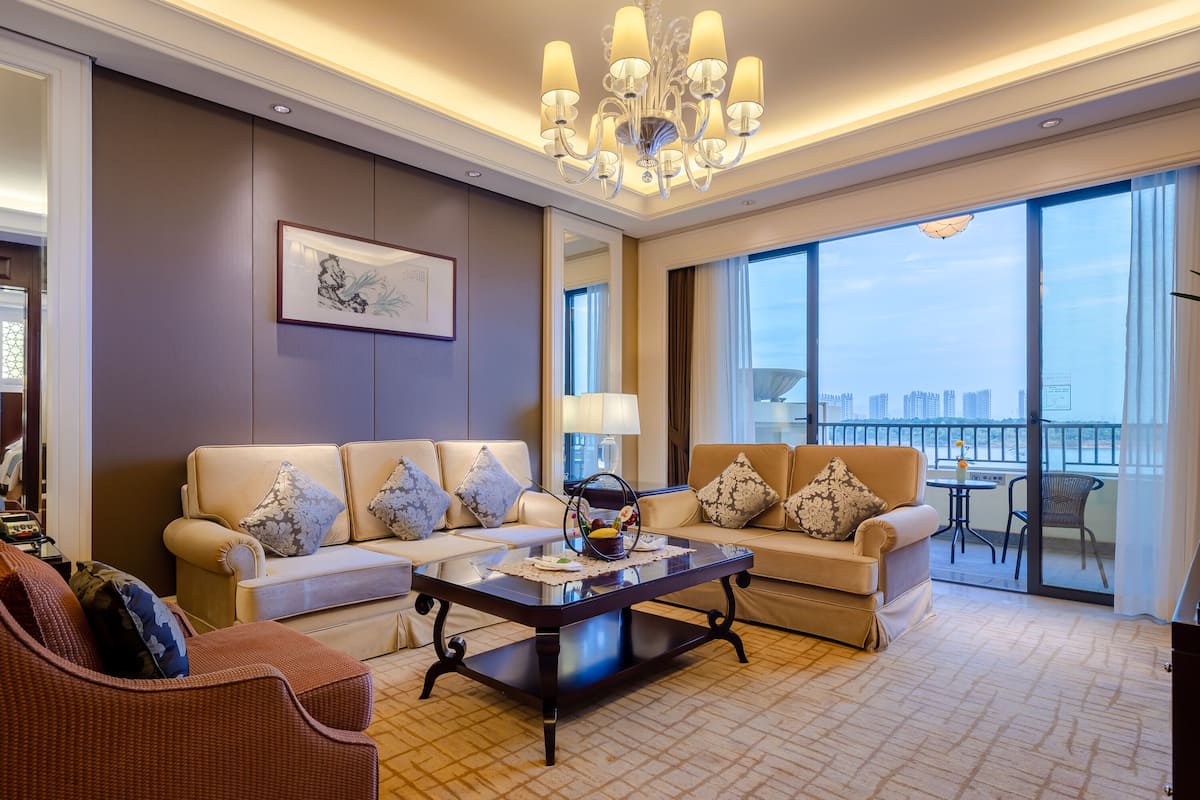 A spacious living room with a large sofa set, a coffee table, and a view of the city through large windows.