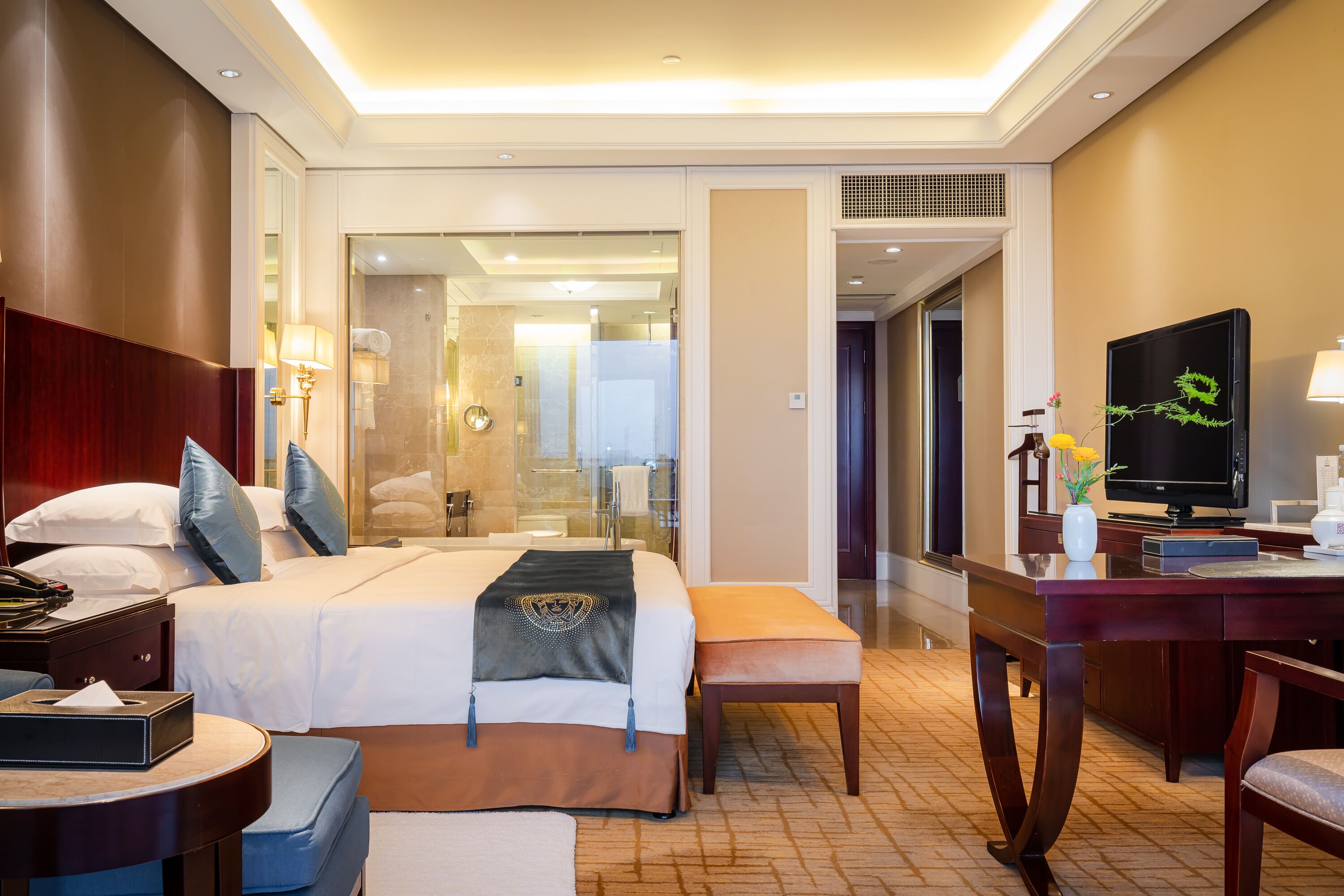 Habitación de hotel con una cama grande, mesitas de noche, un escritorio con silla, televisión y un baño visible a través de una puerta abierta.