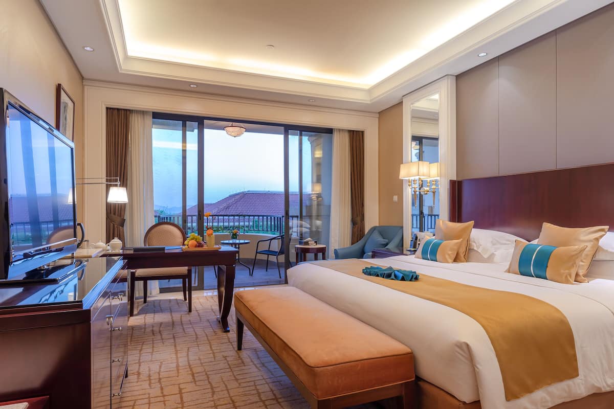 A hotel room with a large bed, a desk, a chair, and a view of the sea.