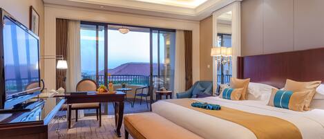 A hotel room with a large bed, a desk, a chair, and a view of the sea.