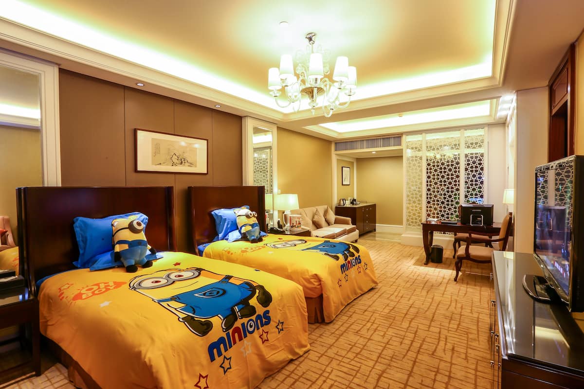 A hotel room with two beds, a TV, a desk, and a chandelier.