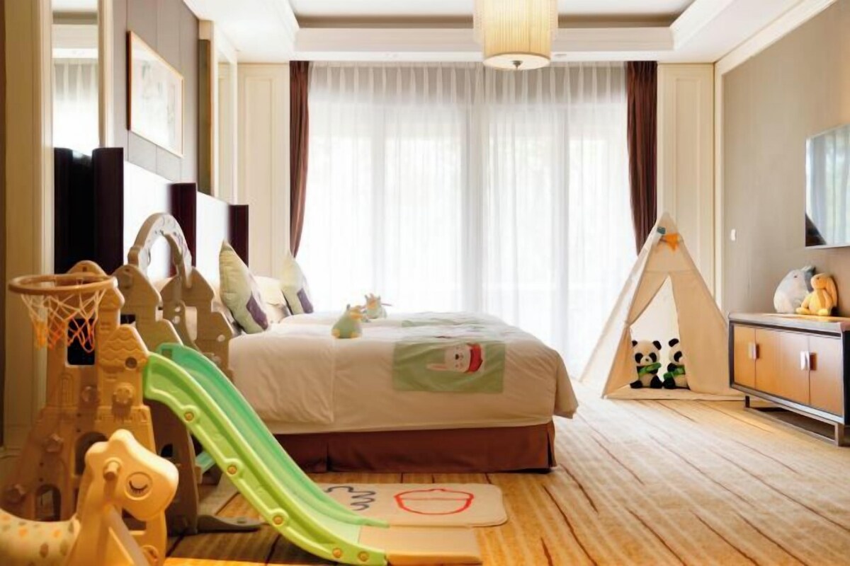 A child-friendly hotel room with a bed, a play area with a slide, a tent, and a television.