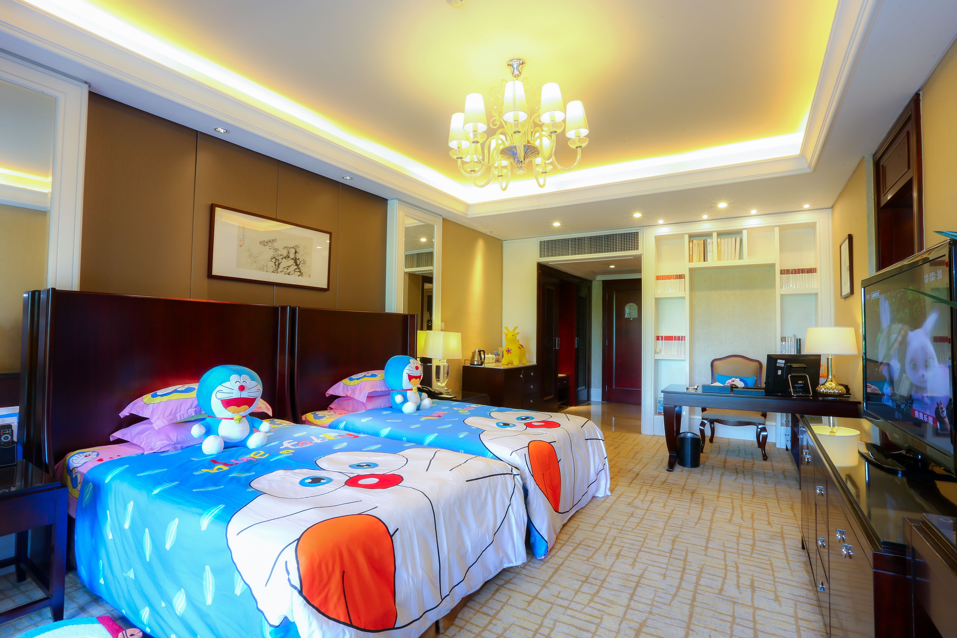 A hotel room with two beds, a television, a desk, and a chandelier.