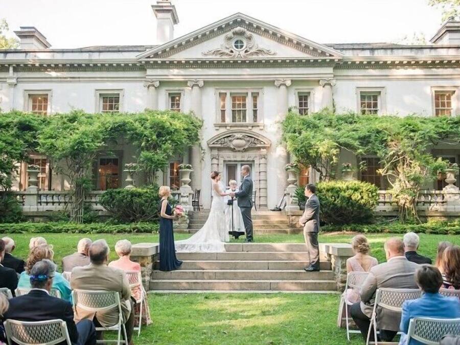Uma cerimônia de casamento em frente a um edifício grande e clássico, com degraus que levam à entrada.
