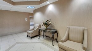 A lobby with a beige carpet, a reception desk, and two beige armchairs.