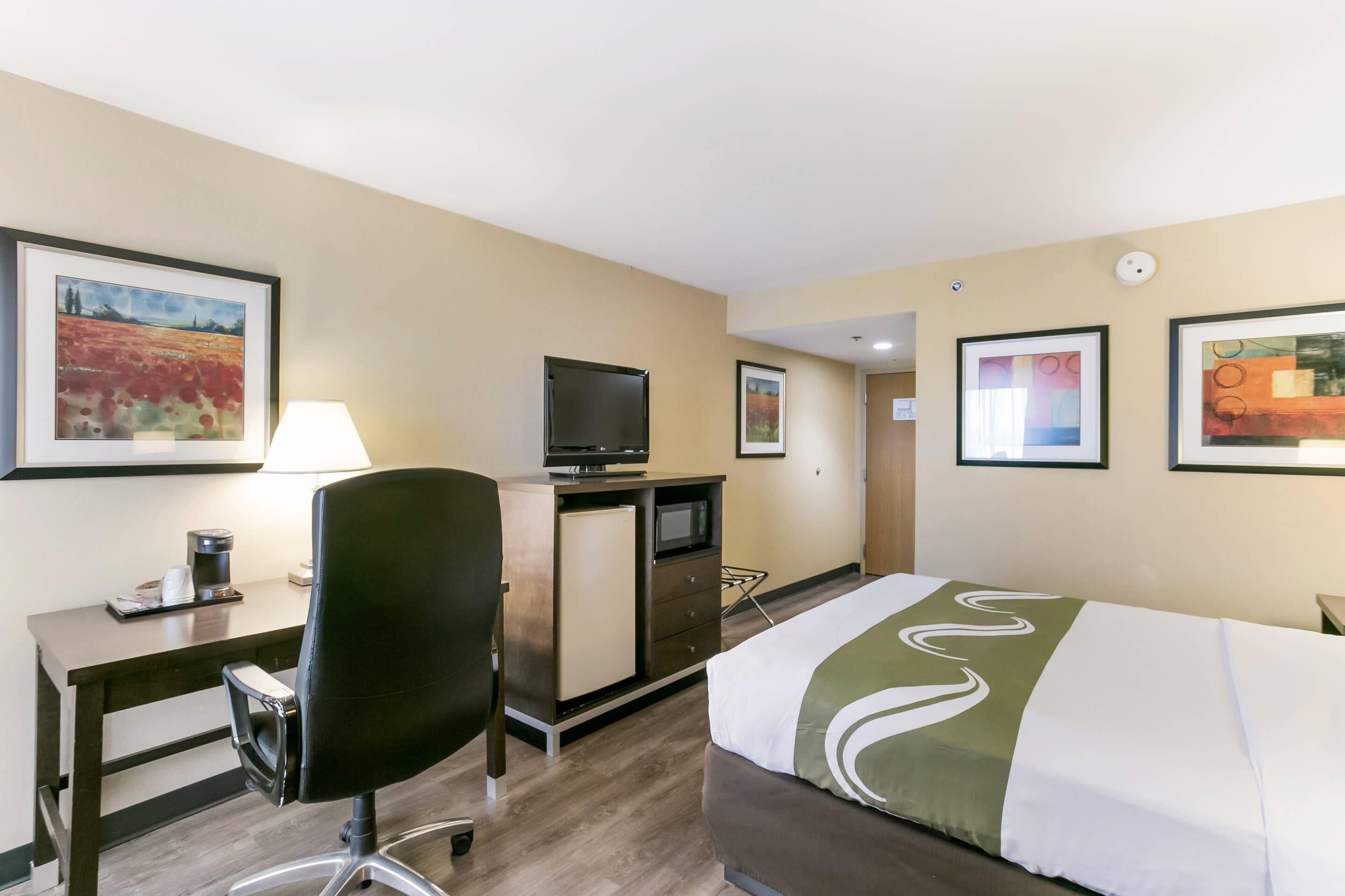 Habitación de hotel con cama, escritorio, silla, televisión y obras de arte en las paredes.