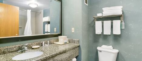 A bathroom with a granite countertop, sink, mirror, and toilet.
