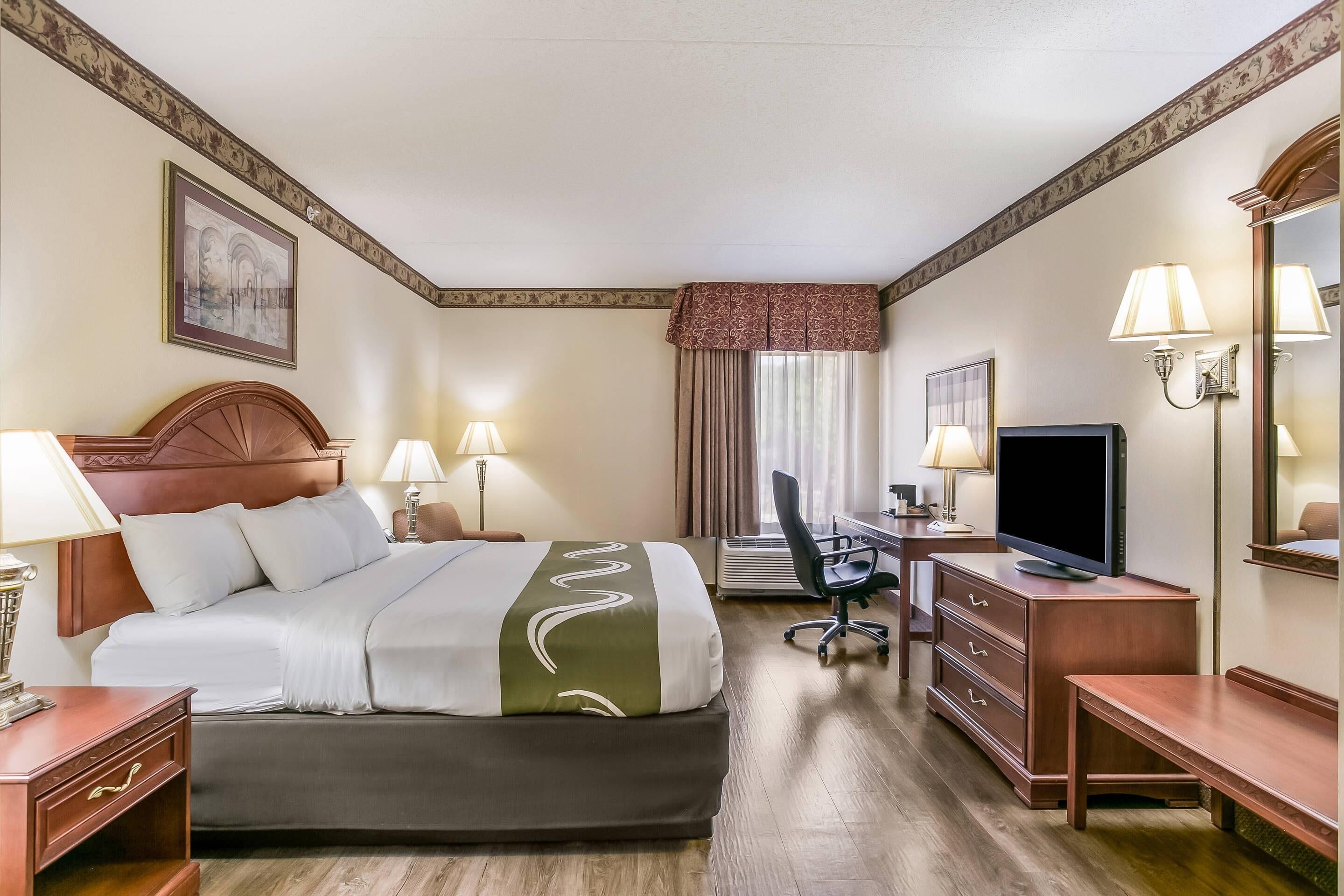 Een hotelkamer met een bed, bureau, televisie en een stoel.