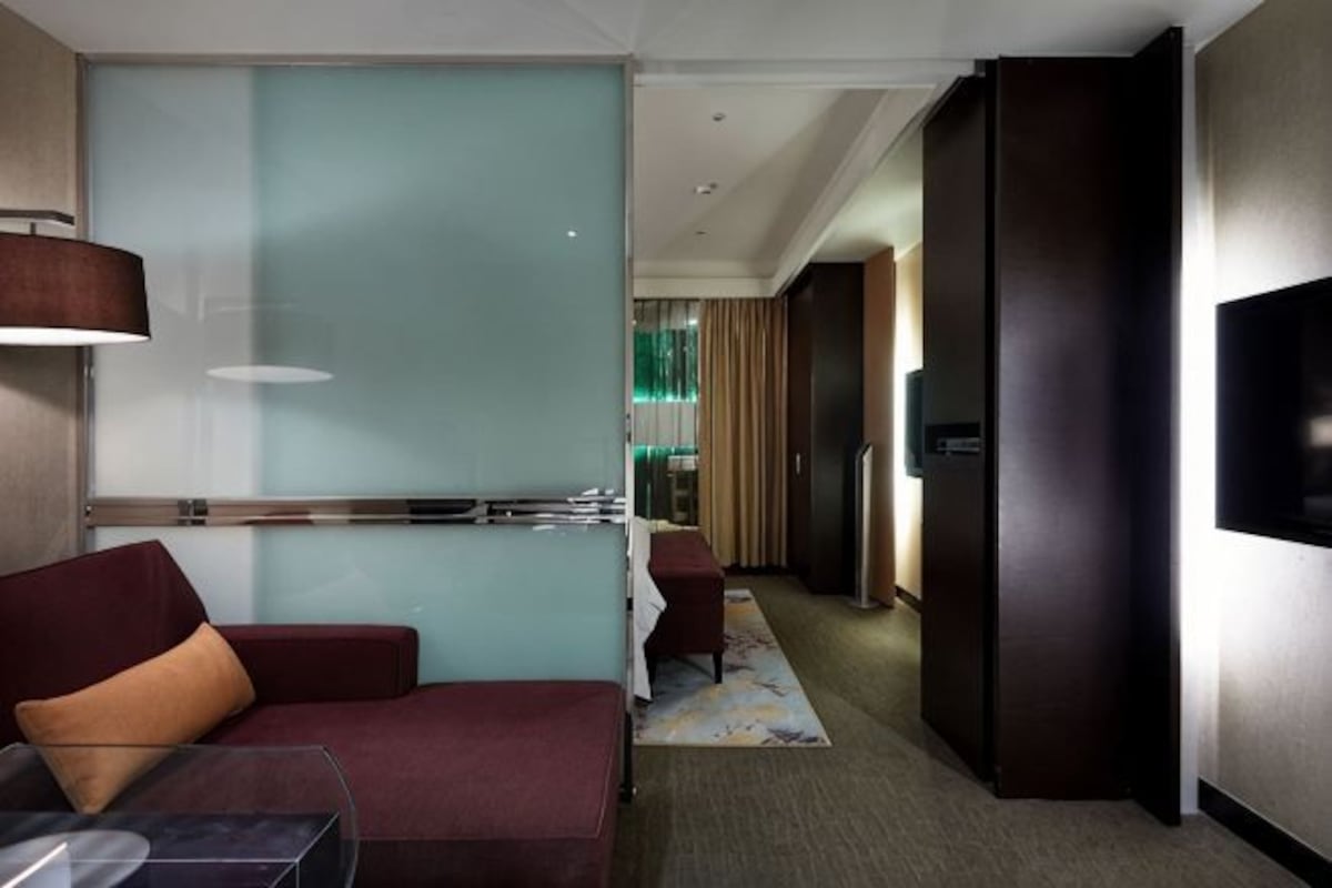 A hotel room with a sofa, a TV, a desk, and a glass partition.