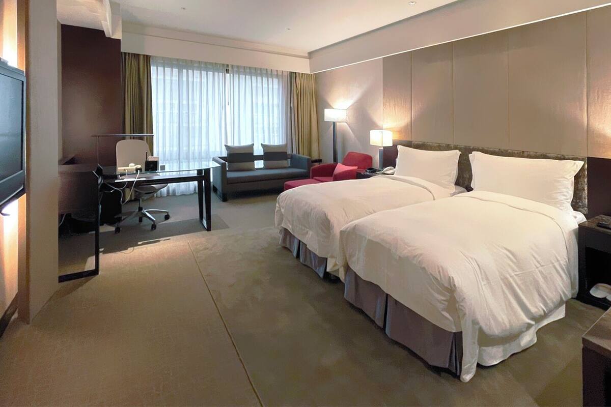 A hotel room with a large bed, a desk, a chair, a TV, and a window with curtains.