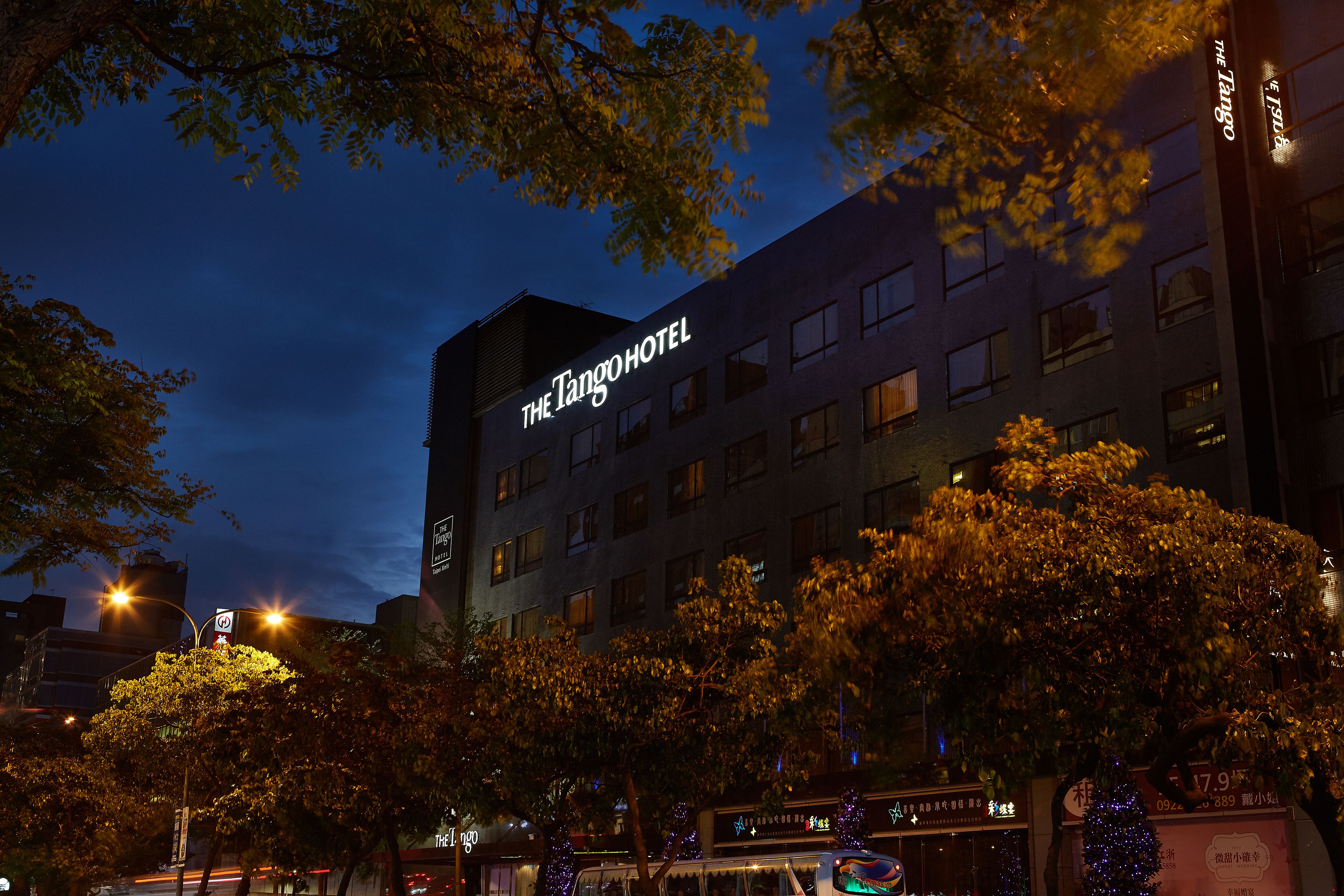 A building with "The Tango Hotel" signage, surrounded by trees and streetlights.