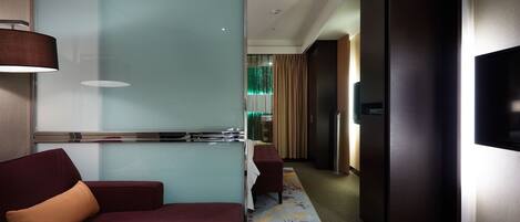 A modern hotel room with a glass partition, a sofa, a small table, and a television.
