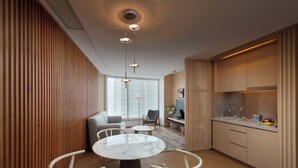 Un salon moderne avec une table en marbre, des chaises blanches, un canapé et un coin cuisine doté de meubles en bois et d’un plan de travail.