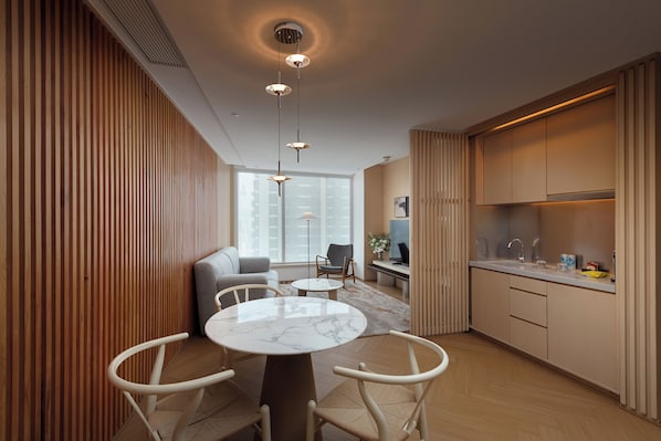 Un salon moderne avec une table en marbre, des chaises blanches, un canapé et un coin cuisine doté de meubles en bois et d’un plan de travail.