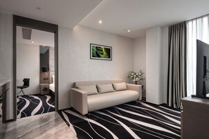 Una habitación de hotel moderna con sofá, televisión de pantalla plana, un cuadro en la pared y alfombra estampada.