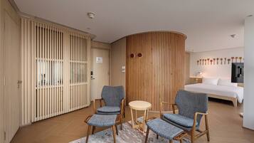 A hotel room with a bed, two armchairs, a small round table, wooden panel walls, and a wooden floor.