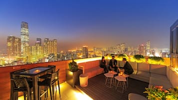 Enjoy breathtaking city views from this rooftop terrace with a glass-top table, two chairs, a sofa, and potted plants.