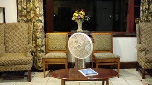 A living room with two patterned armchairs, a wooden coffee table, and a standing fan. - Driftwood Inn (Chestertown)