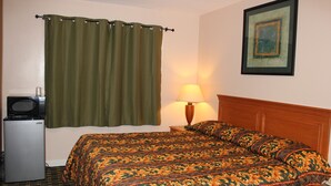 A hotel room with a bed, a small refrigerator, a lamp, a picture on the wall, and a curtain. - Driftwood Inn (Chestertown)