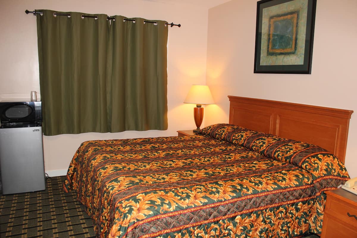 A hotel room with a bed, a nightstand with a lamp, a small refrigerator, and a curtain.