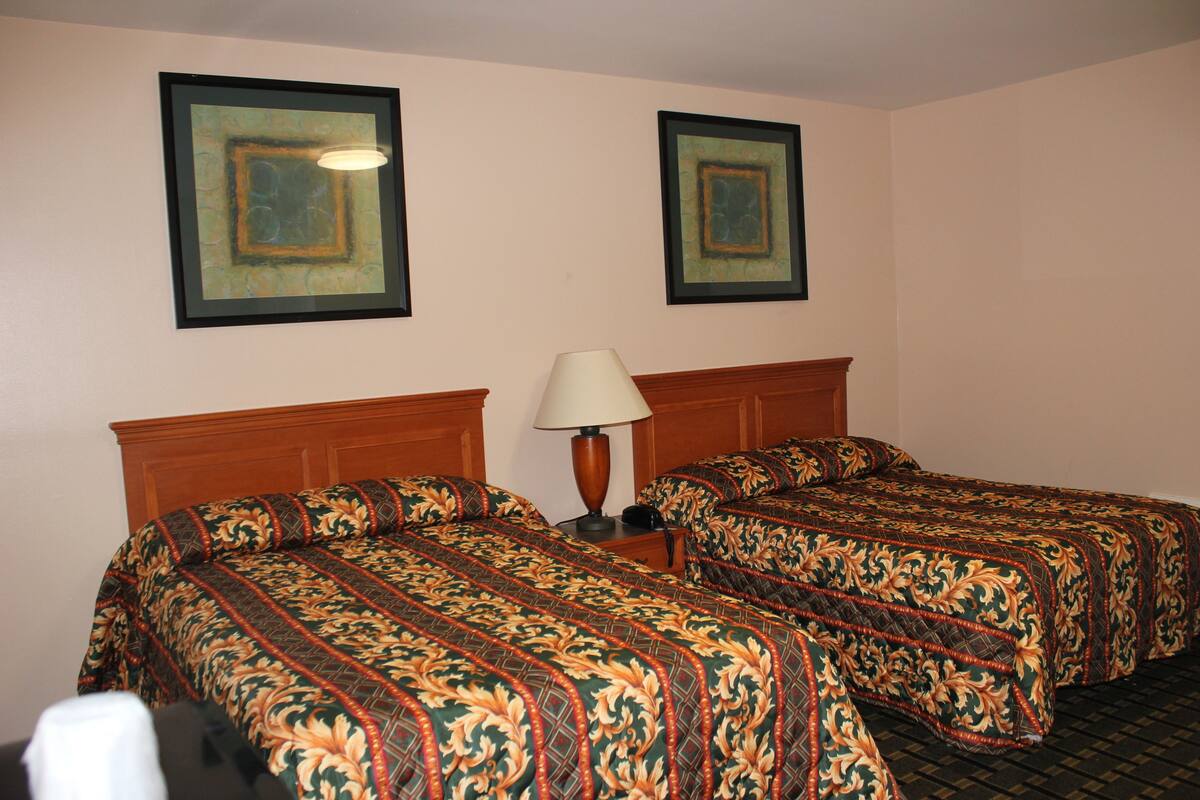 A hotel room with two beds, a nightstand, a lamp, and two framed pictures on the wall.