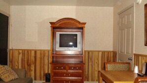 A living room with a wooden cabinet, a television, a sofa, and a dining table. - Driftwood Inn (Chestertown)