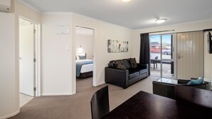 A hotel room with a bed, a sofa, a dining table, and a view of the outside. - ASURE Aveda Motor Lodge (Pukekohe)