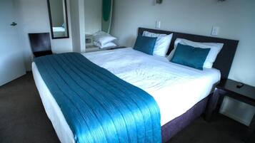 Una habitación de hotel con una cama grande, una mesita de noche, una silla y un espejo.