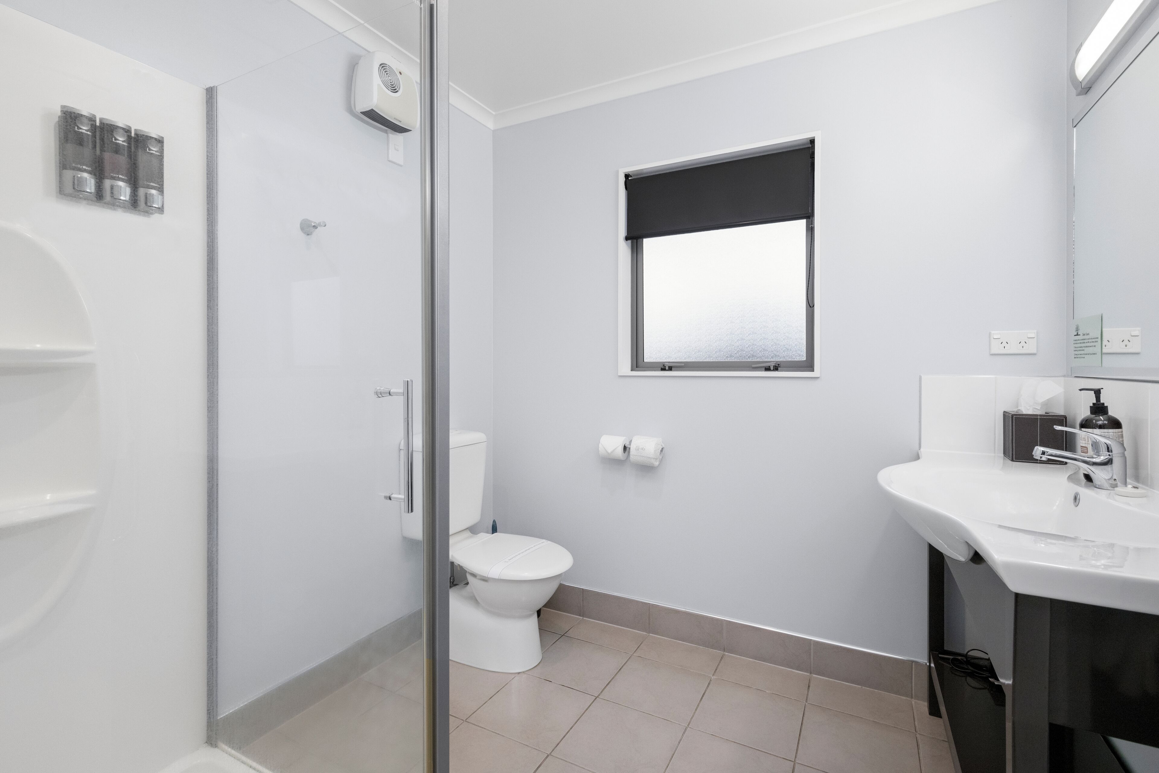 A modern bathroom with a glass shower enclosure, a toilet, a sink with a mirror, and a window.