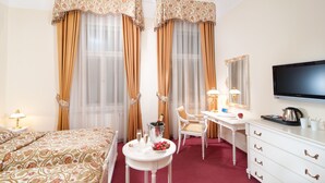 A hotel room with a bed, a desk, a television, and a minibar. - Alqush Downtown Hotel (Prague)