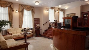 A spacious living room with a sofa, coffee table, and a wooden reception desk. - Alqush Downtown Hotel (Prague)