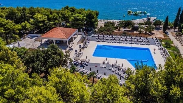 A resort with a swimming pool, lounge chairs, and a view of the sea. -  Hotel Medena Budget (Seget)
