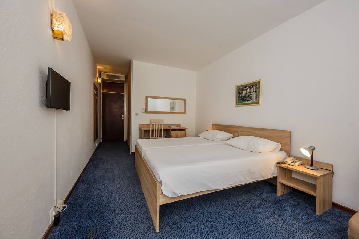 Una habitación de hotel con cama, mesita de noche, lámpara y televisor montado en la pared.