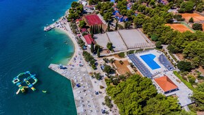 An aerial view of a coastal area with a beach, a swimming pool, and a tennis court. -  Hotel Medena Budget (Seget)