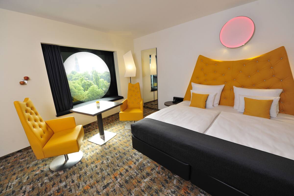 Habitación de hotel con cama, escritorio, silla y un amplio ventanal con vistas.