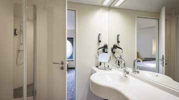 A modern bathroom with a glass-enclosed shower, a large sink with dual faucets, and a mirror with a light.