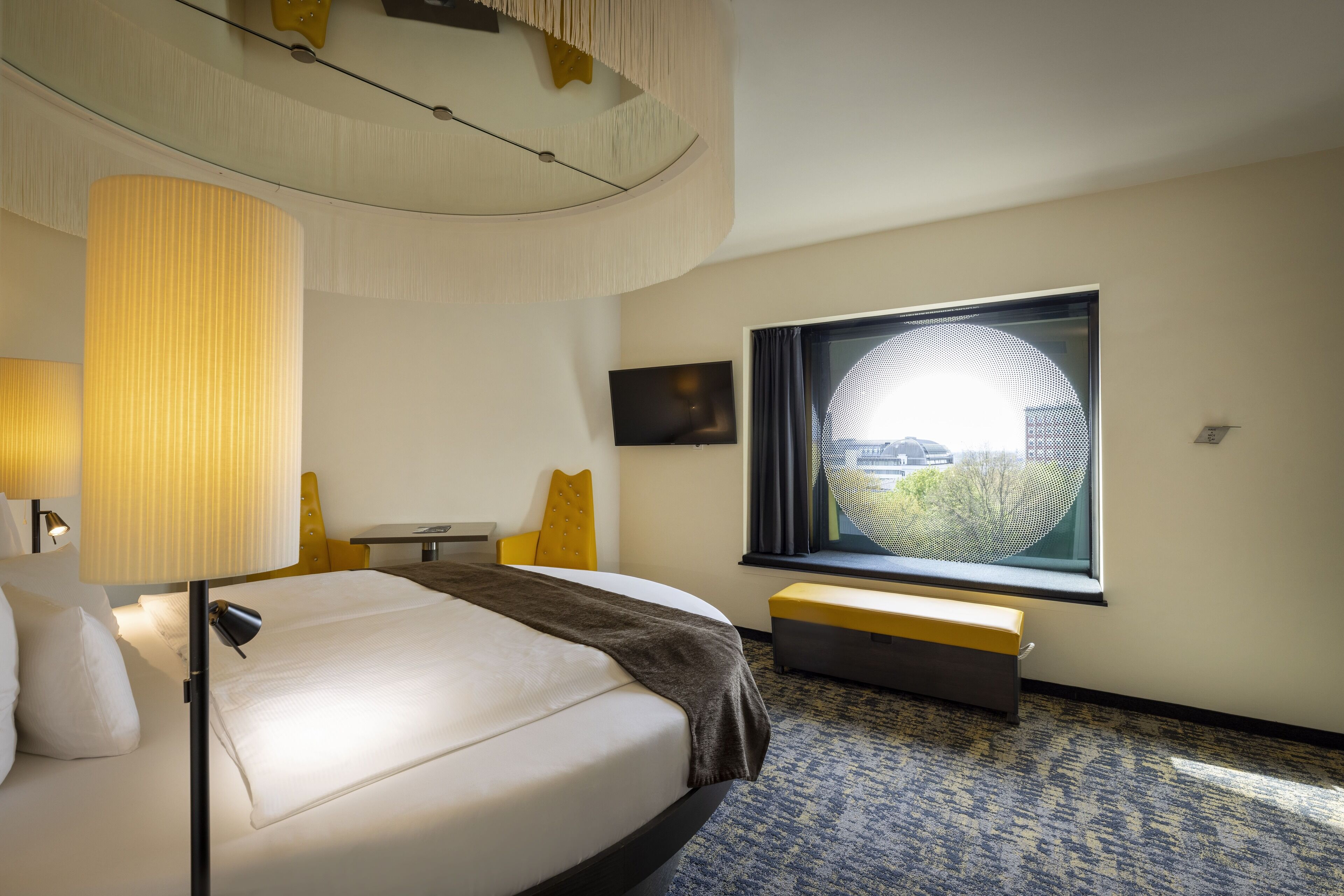 Hotelkamer met een groot bed, een bureau, een stoel, een bankje, een televisie en een raam met uitzicht.