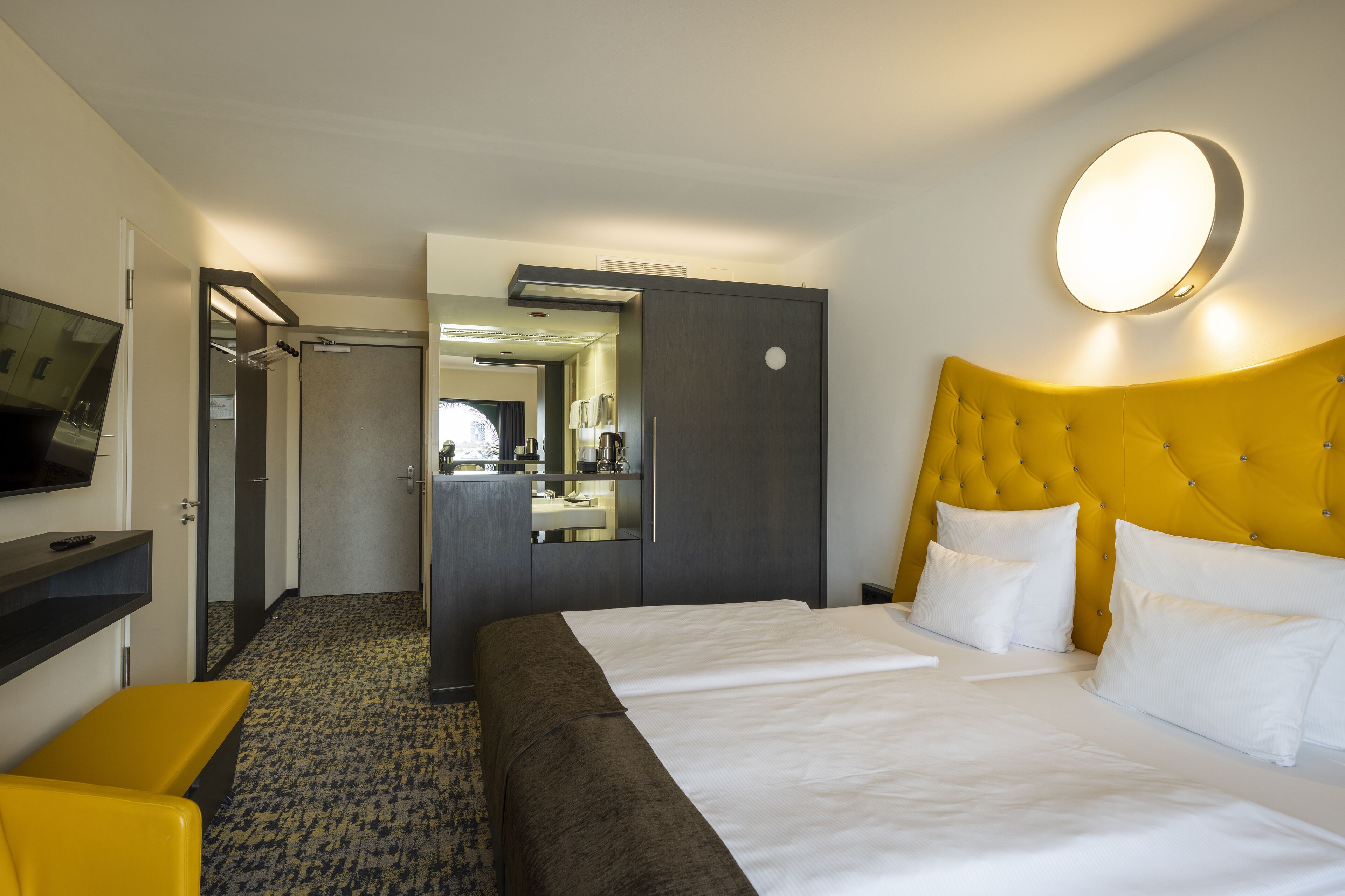 Une chambre d’hôtel avec un grand lit, un téléviseur posé sur un meuble, un miroir et une porte donnant sur la salle de bain.