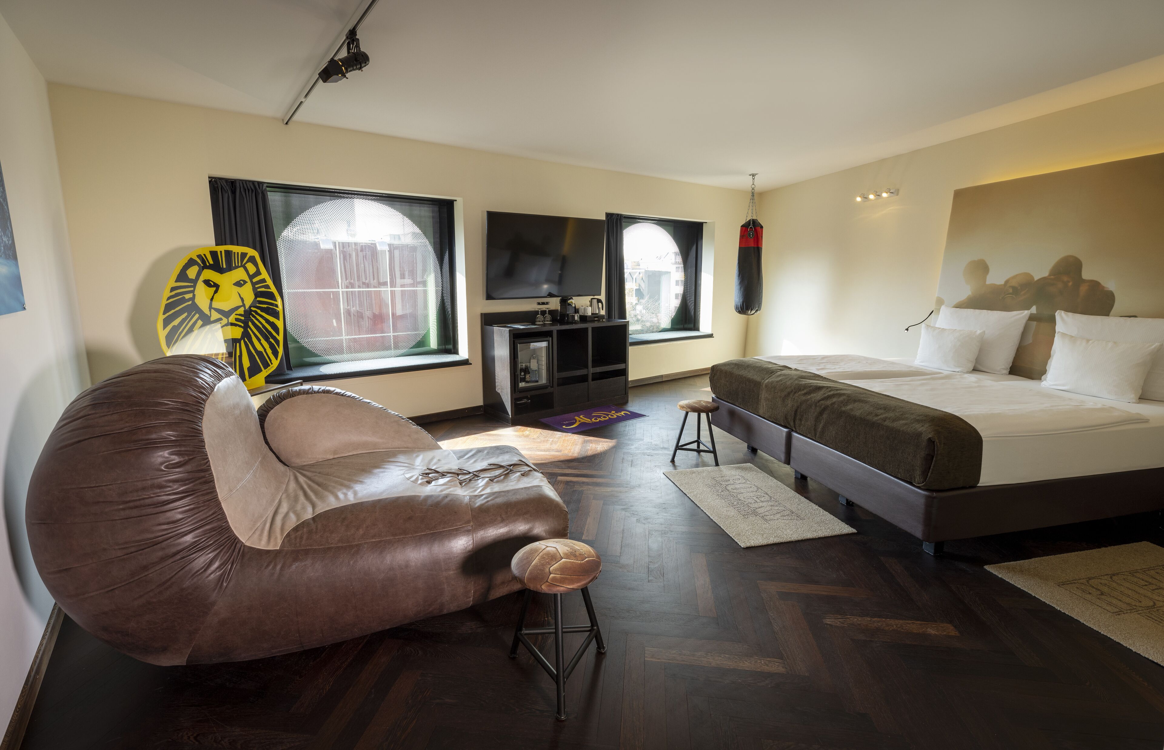 Una habitación de hotel moderna con una cama grande, un sofá de cuero, un televisor y un saco de boxeo.