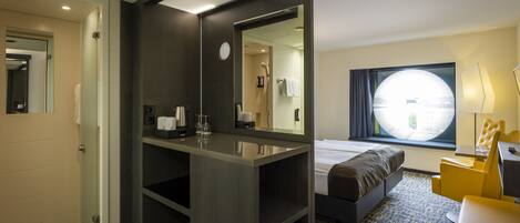 A modern hotel room with a large bed, a bedside table, a mirror, a window with a view, and a small seating area.