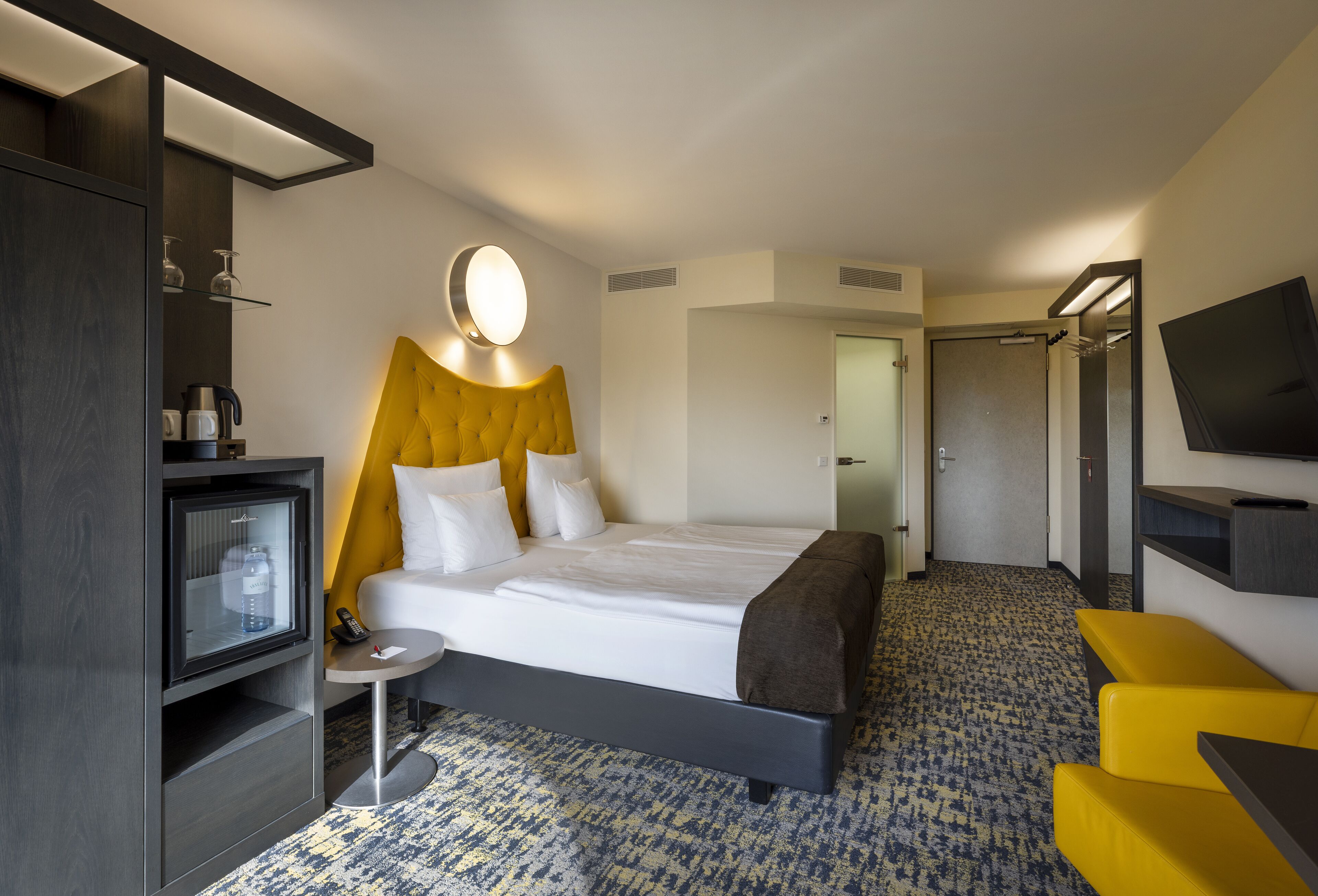A hotel room with a bed, a small table, a TV, a mirror, and a wardrobe.