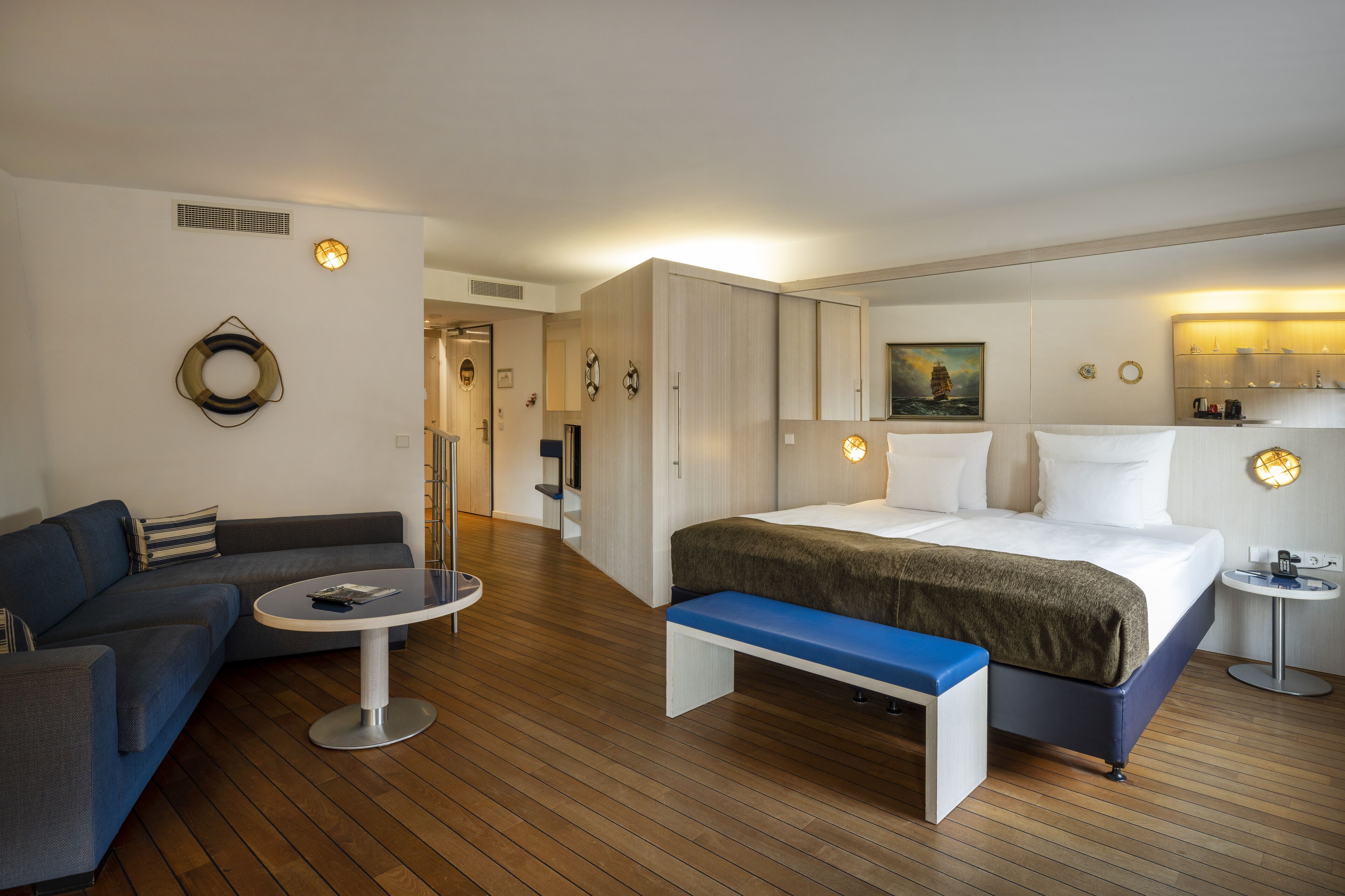A modern hotel room with a bed, a sofa, a small round table, and a bench.