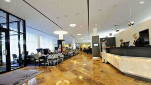 A hotel lobby with a marble floor, a reception desk, and a seating area with tables and chairs.