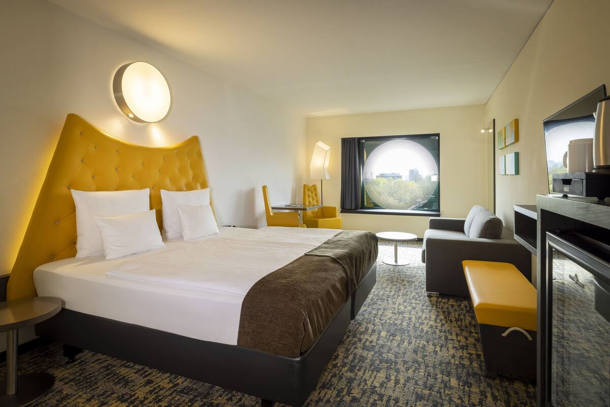 Habitación de hotel con una cama grande, un escritorio, una silla, un sofá y vistas al exterior.