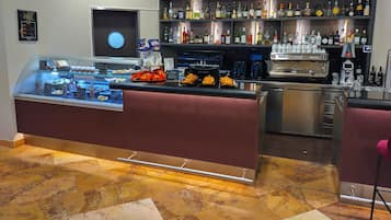 Zona de bar con varias botellas de licores, una máquina de café y una vitrina con pasteles.