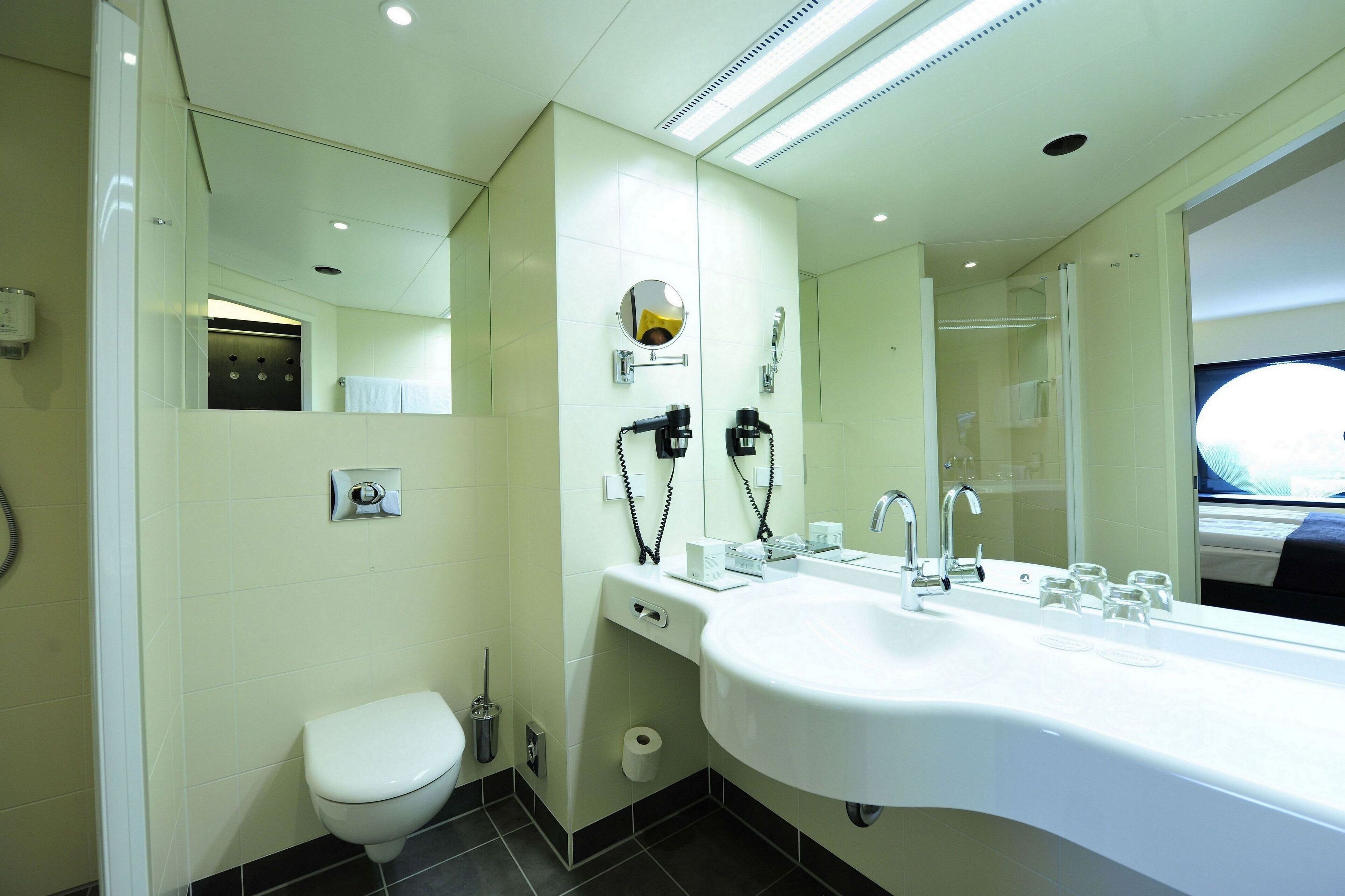 A modern bathroom with a white sink, a large mirror, a toilet, and a shower area.
